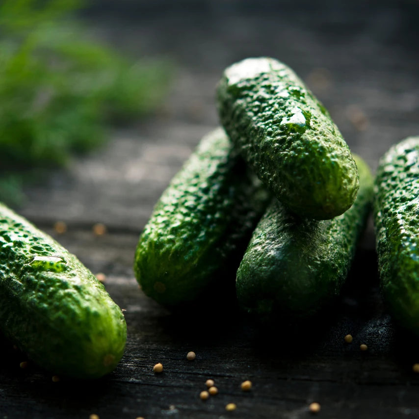 Green cucumbers on a wooden surface with mustard seeds.