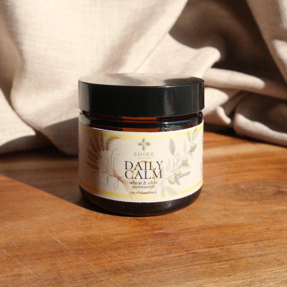 Jar of 'Daily Calm' wheat and olive moisturizer on a wooden surface with a neutral background