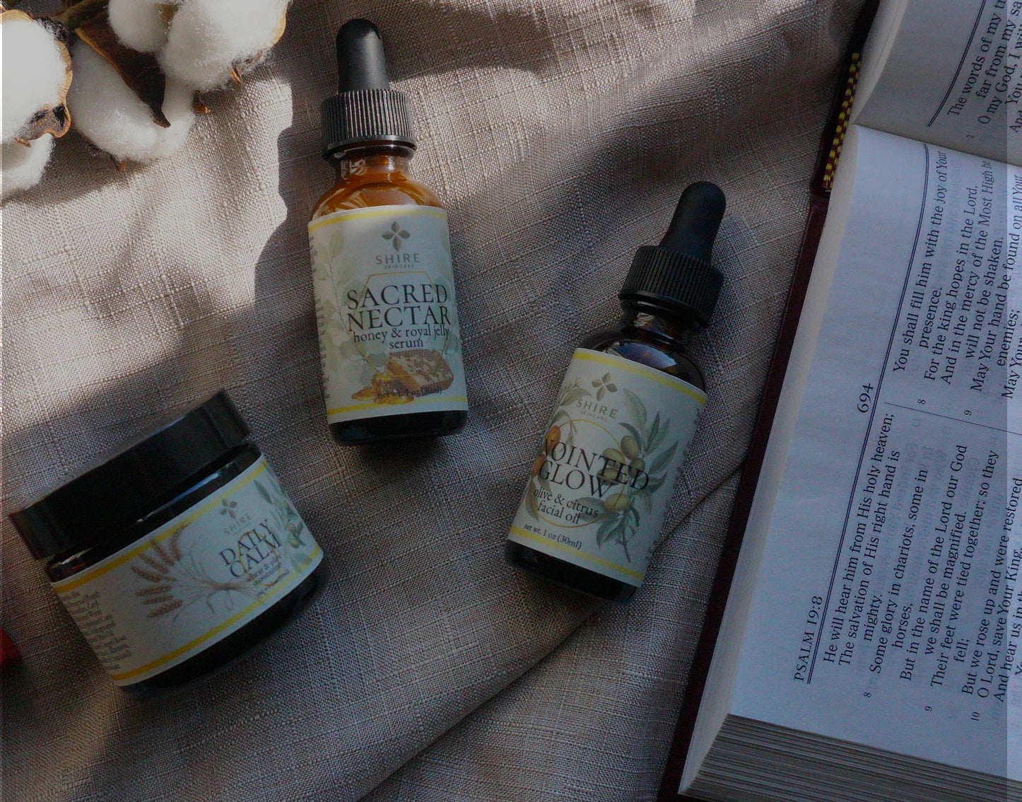 Biblical skincare products in amber glass bottles, laying on a linen surface with a Bible opened to Psalm 19