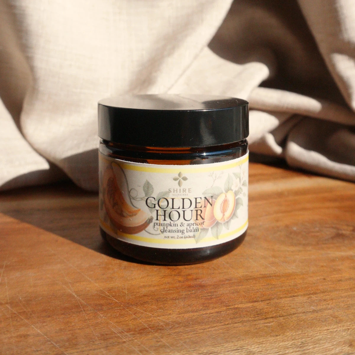 Jar of 'Golden Hour' pumpkin and apricot cleansing balm on a wooden surface with a beige fabric background