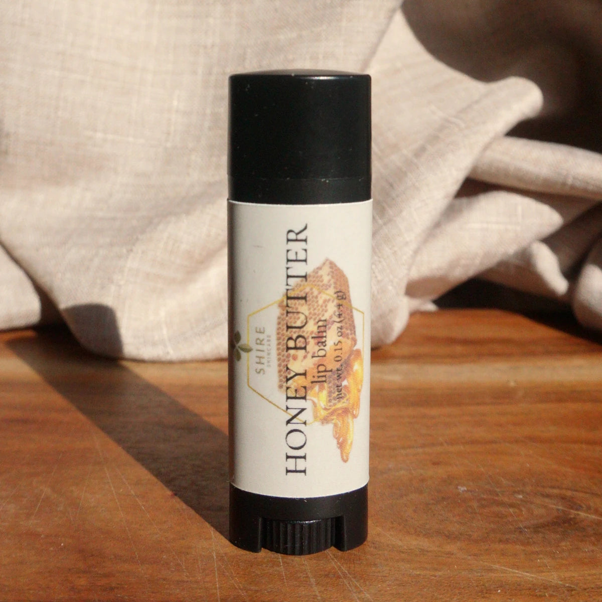 Honey Butter lip balm on a wooden surface with a soft fabric background