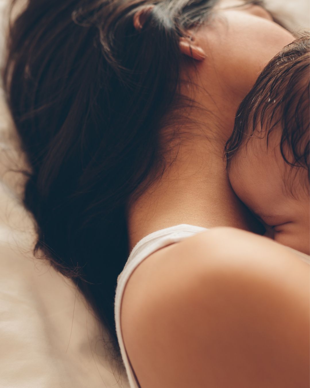 Close-up of a mother and baby lying down with a neutral background.