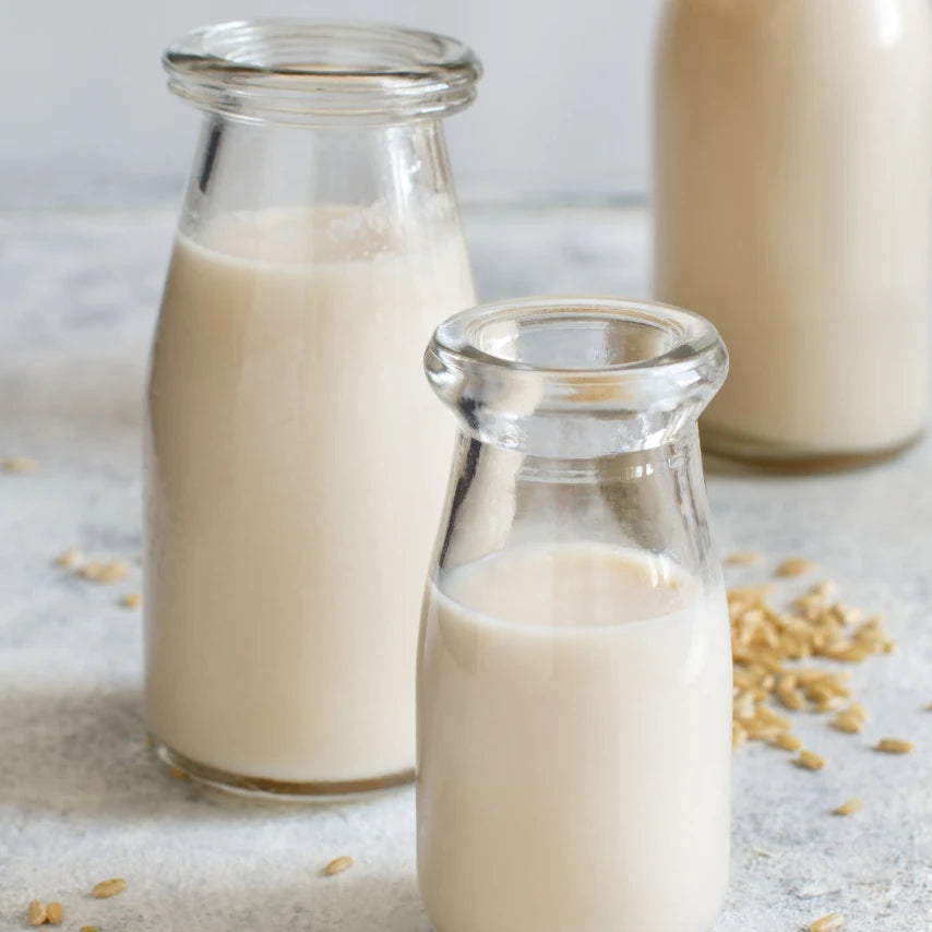Three glass bottles of milk on a light background with scattered oats.
