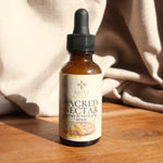 Bottle of Shire Skincare's Sacred Nectar honey & royal jelly serum on a wooden surface with a beige cloth in the background.