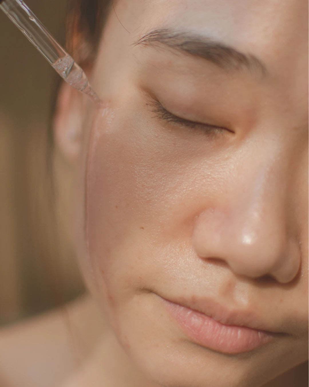 Close-up of a person's face with a dropper near their eye, applying serum.