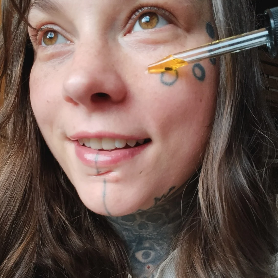 Woman applying a biblical skincare product called "Anointed Glow" facial oil to her face with a dropper.