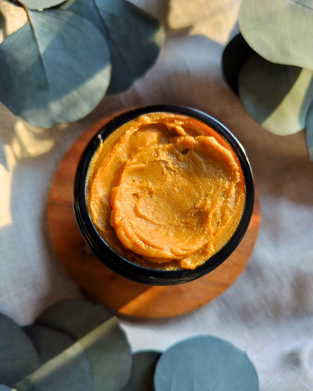 Close-up of a container with pumpkin colored balm on a textured surface.