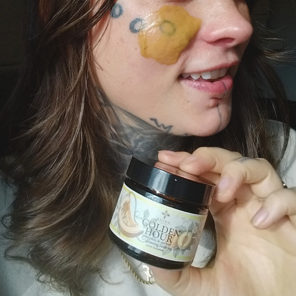 Person holding a jar of 'The Golden Hour' cleansing balm with a swipe of product on their face, showcasing biblical skincare.