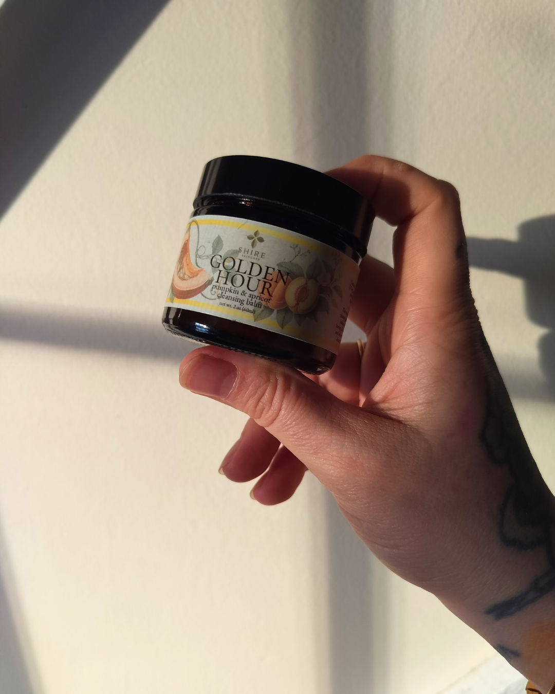 Hand holding a jar of 'Golden Hour' product against a light background