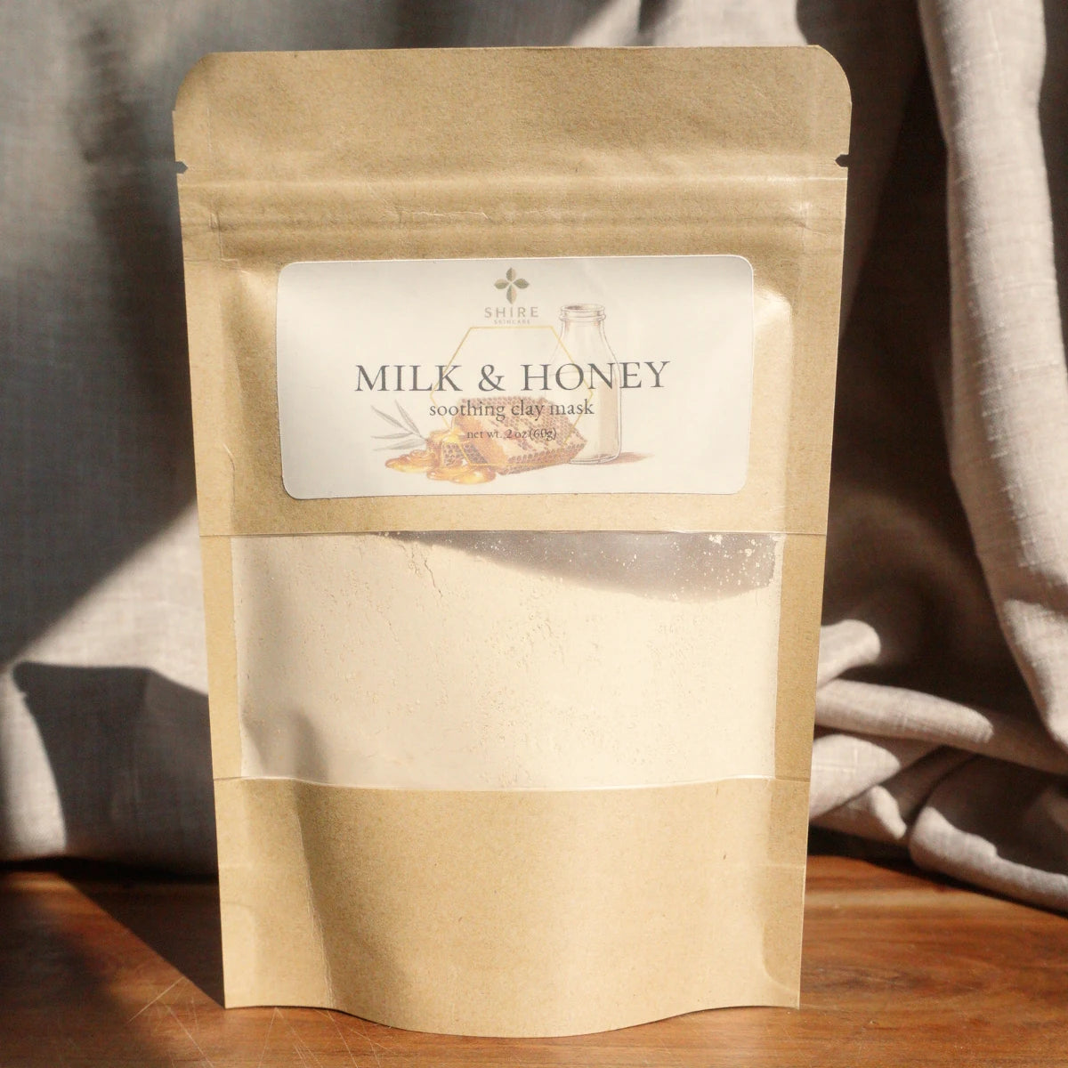Kraft paper packaging of 'Milk & Honey' soothing clay mask product on a wooden surface with a neutral background