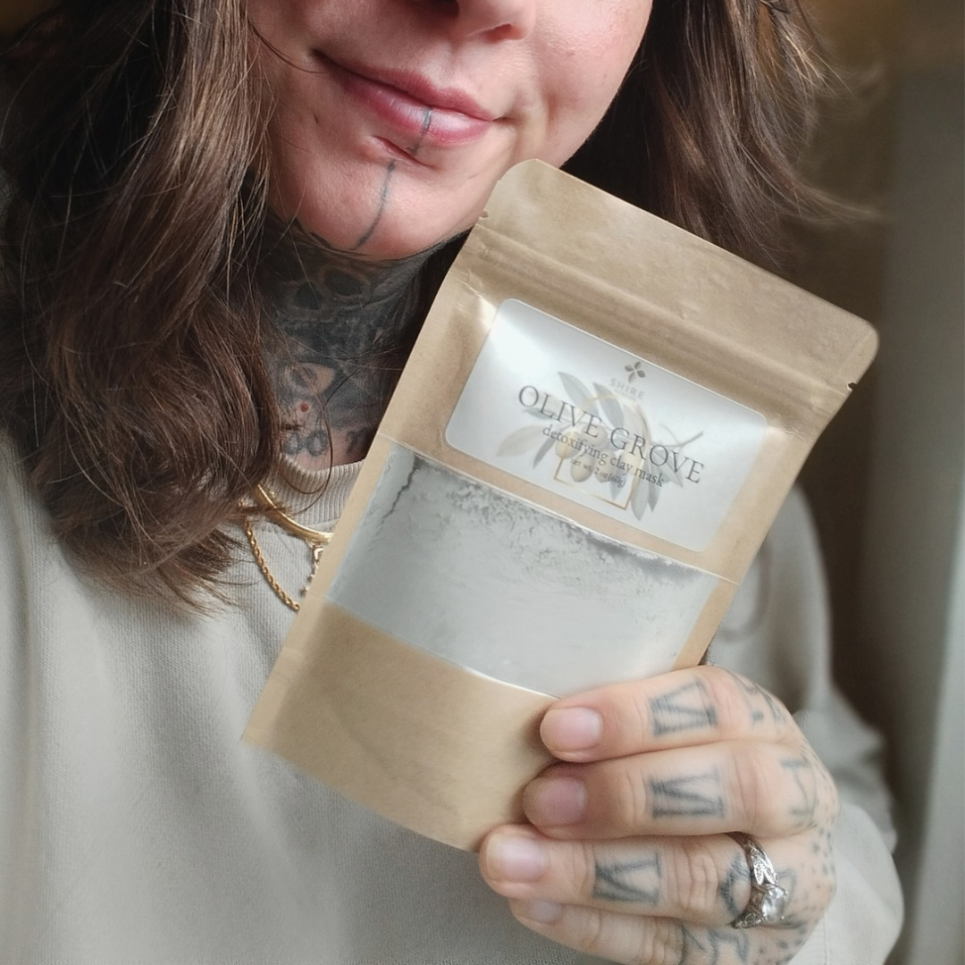 Person holding a brown paper pouch with 'Olive Grove' clay mask label