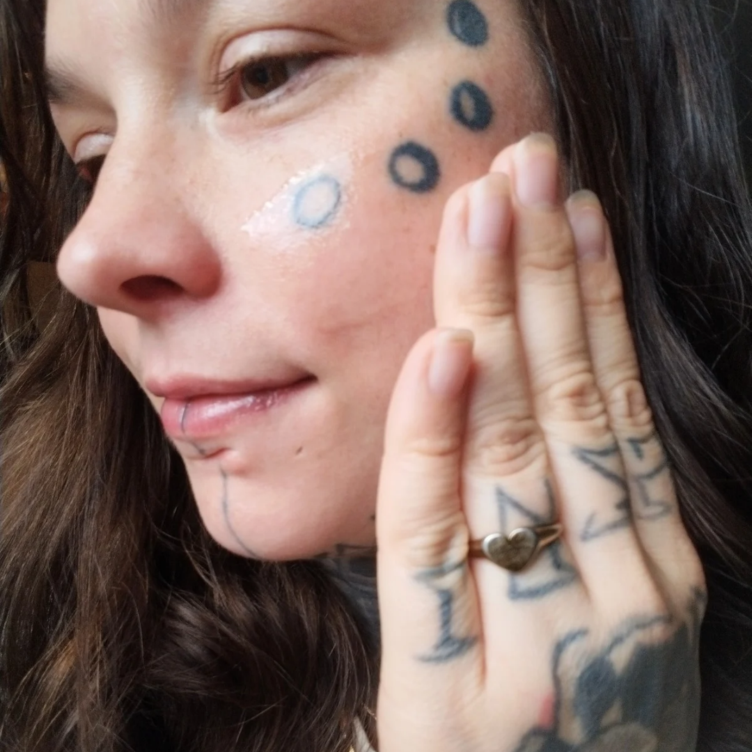 Close-up of a person applying biblical skincare product called "Sacred Nectar Serum" to their face.