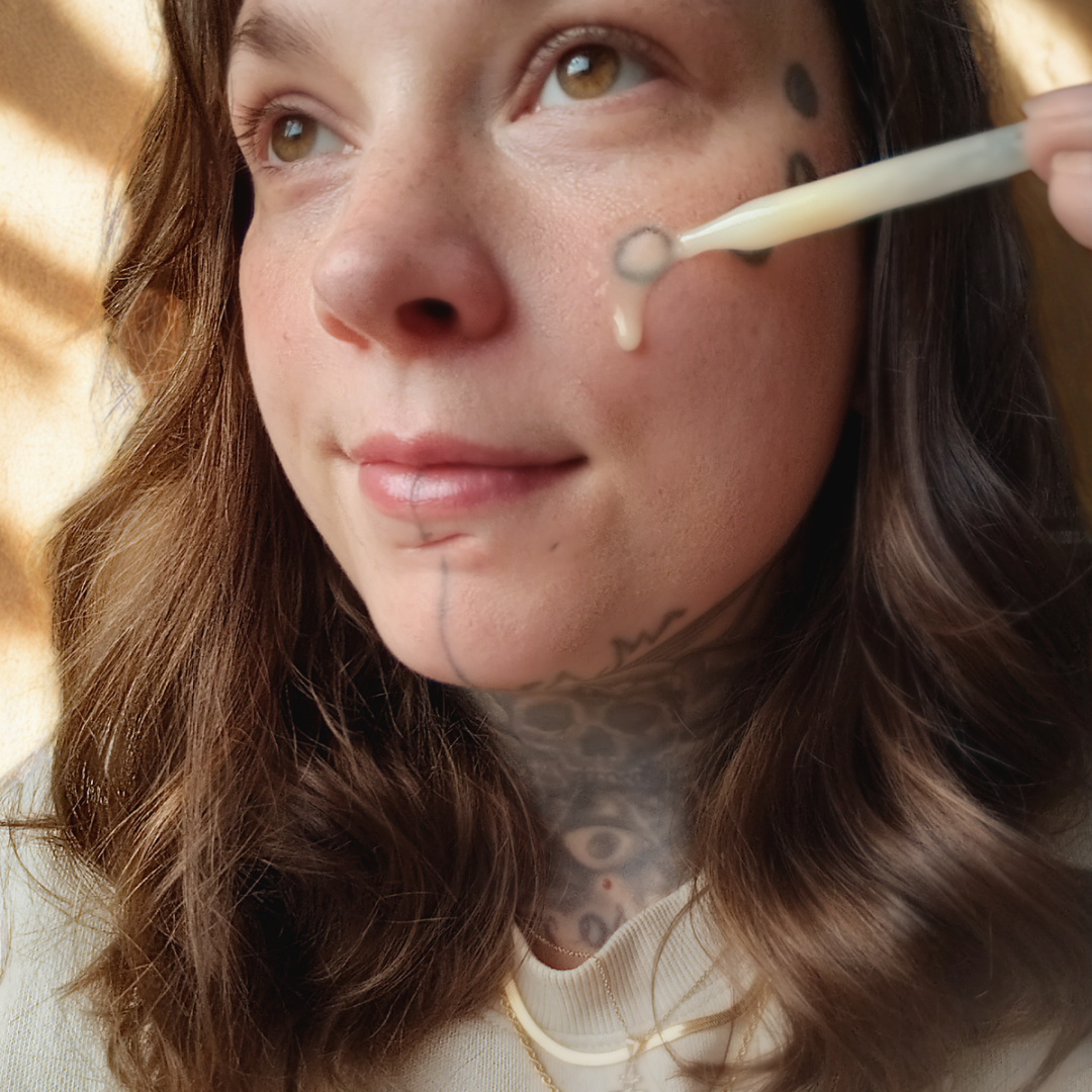 Person applying biblical skincare product called "Sacred Nectar" serum to their face with a dropper, surrounded by warm lighting.