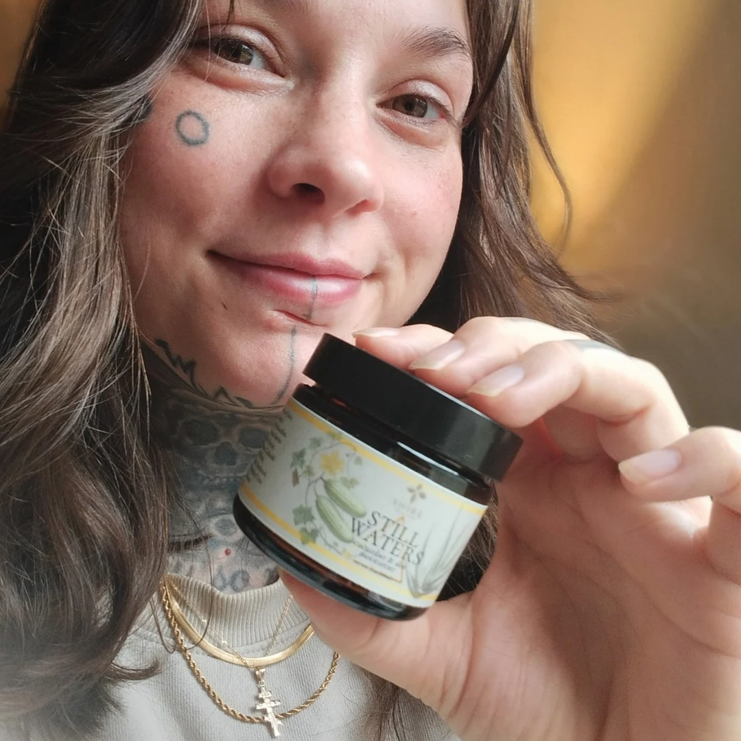 Person holding a biblical skincare jar labeled 'Still Waters' with a blurred background