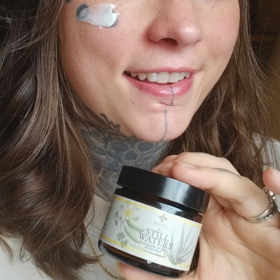 Person holding a jar of biblical skincare called 'Still Waters' moisturizer with product applied to cheek